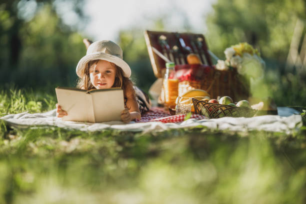 A Cute Smiling Spending A Spring Day In Nature And Reading Book On Picnic.
