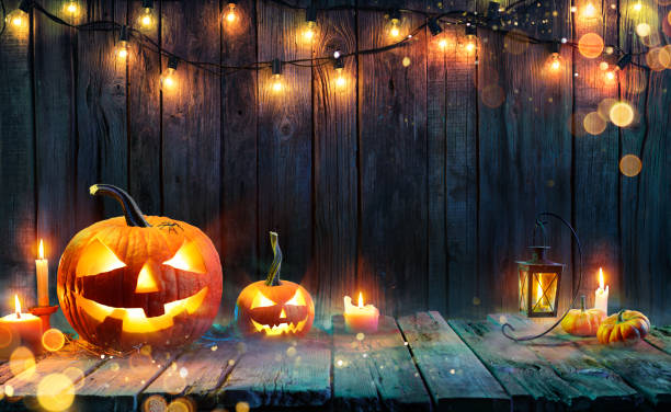 Halloween Jack O' Lanterns Candles And String Lights On Wooden Table