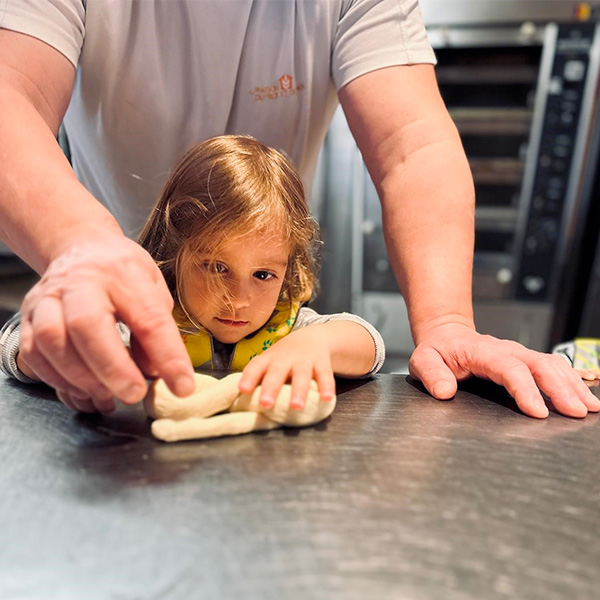 Enfant façonnant une tresse de pain avec l’aide d’un boulanger