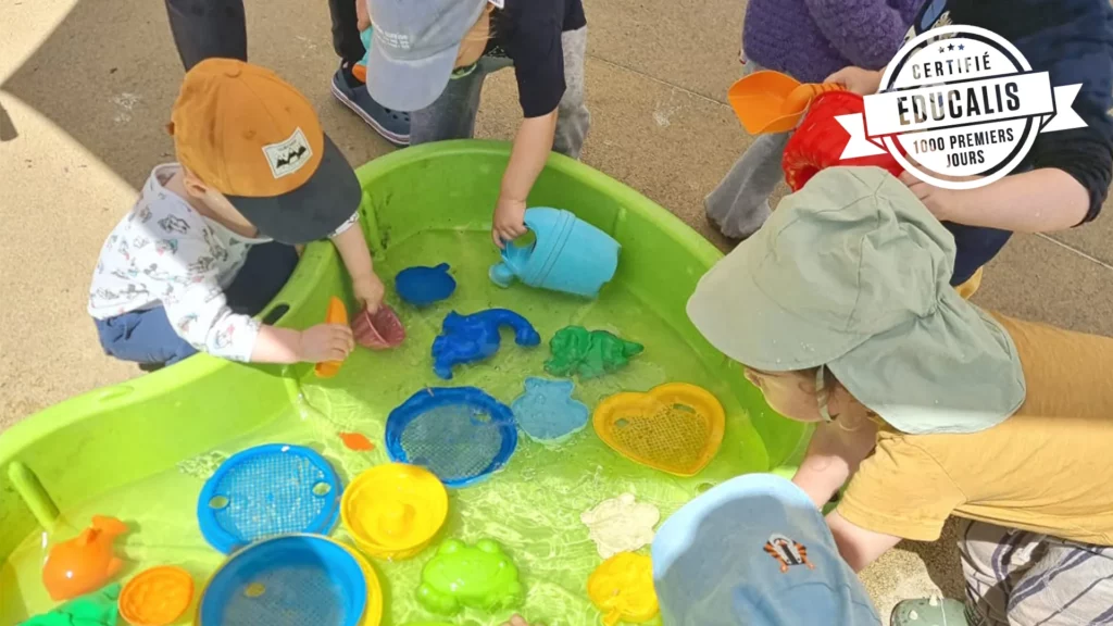 Vue du jardin avec le grand bassin de jeux d’eau et les enfants concentrés autour.
