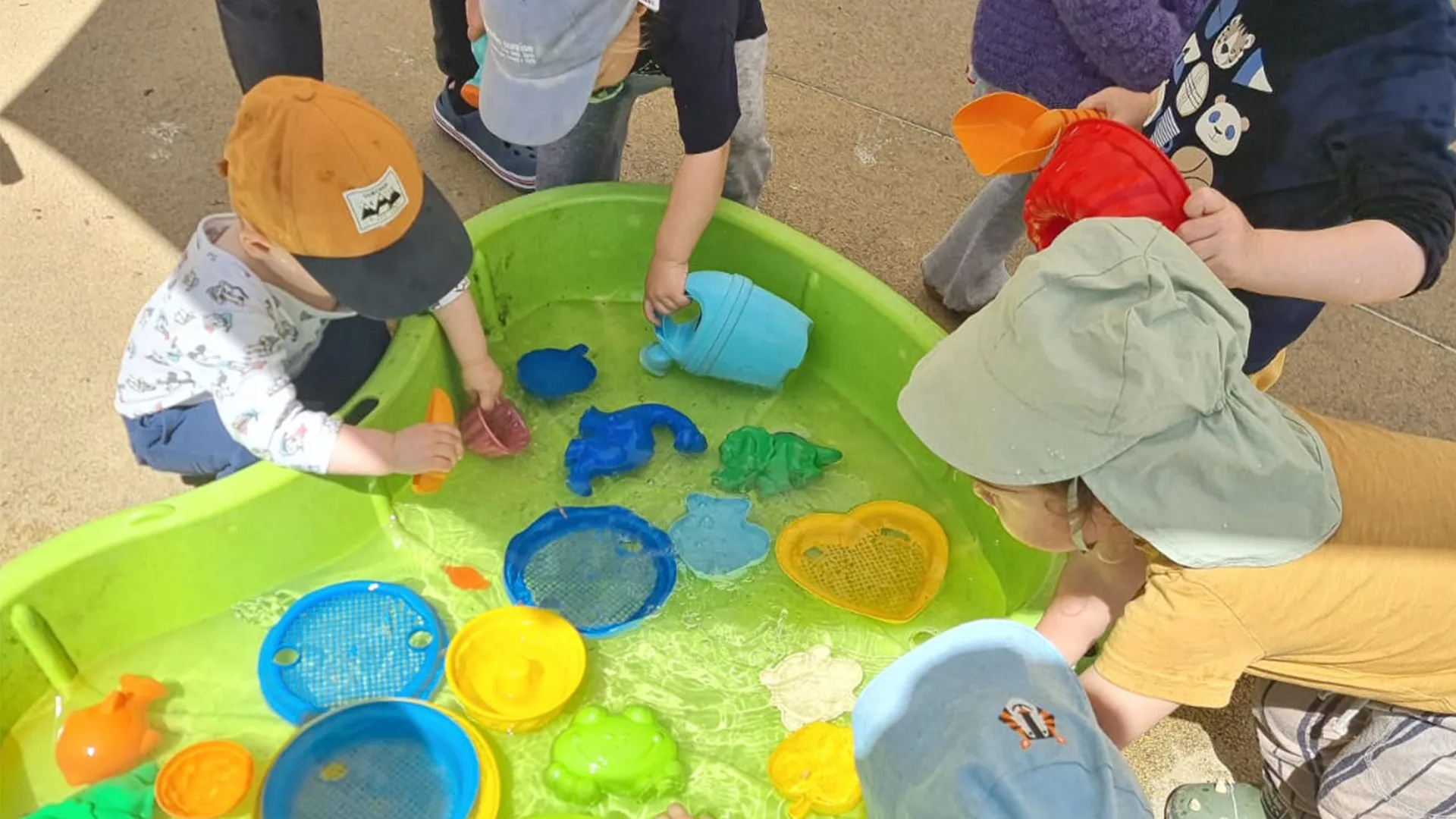 Vue du jardin avec le grand bassin de jeux d’eau et les enfants concentrés autour.