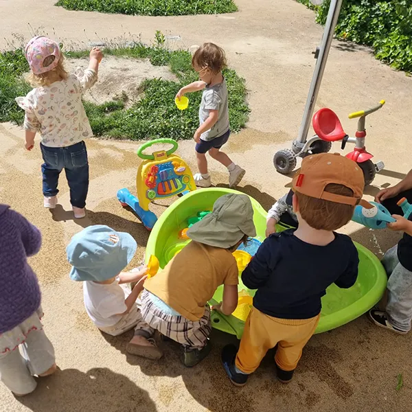 Vue du jardin avec le grand bassin de jeux d’eau et les enfants concentrés autour.