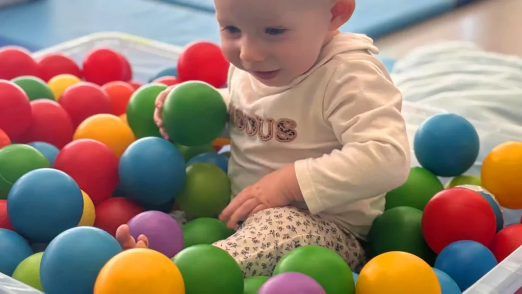 Enfant souriant qui colle des balles colorées sur un cerceau adhésif à la crèche Le Microcosme à Lausanne.